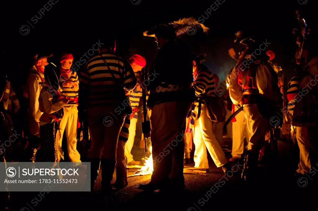 People collecting around small fire during a break in procession at East Hoathly Bonfire Night; East Sussex, England