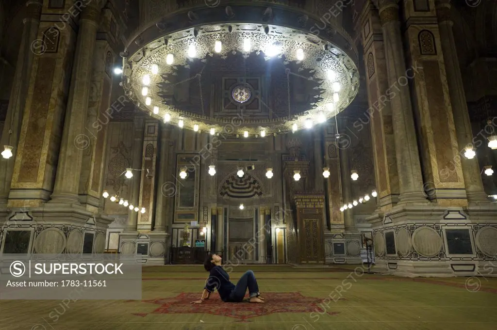 Woman meditating under chandelier in temple, Cairo, Egypt.