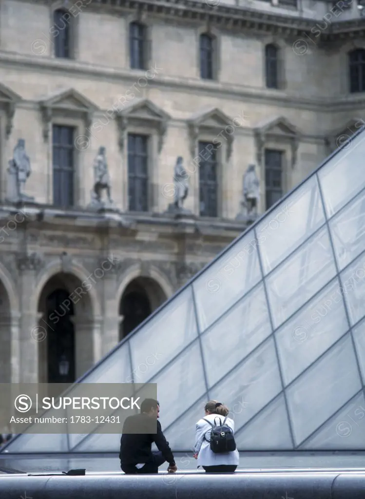 Young couple beside the pyramid in the courtyard of Louvre, Paris, Ile-de-France, France.