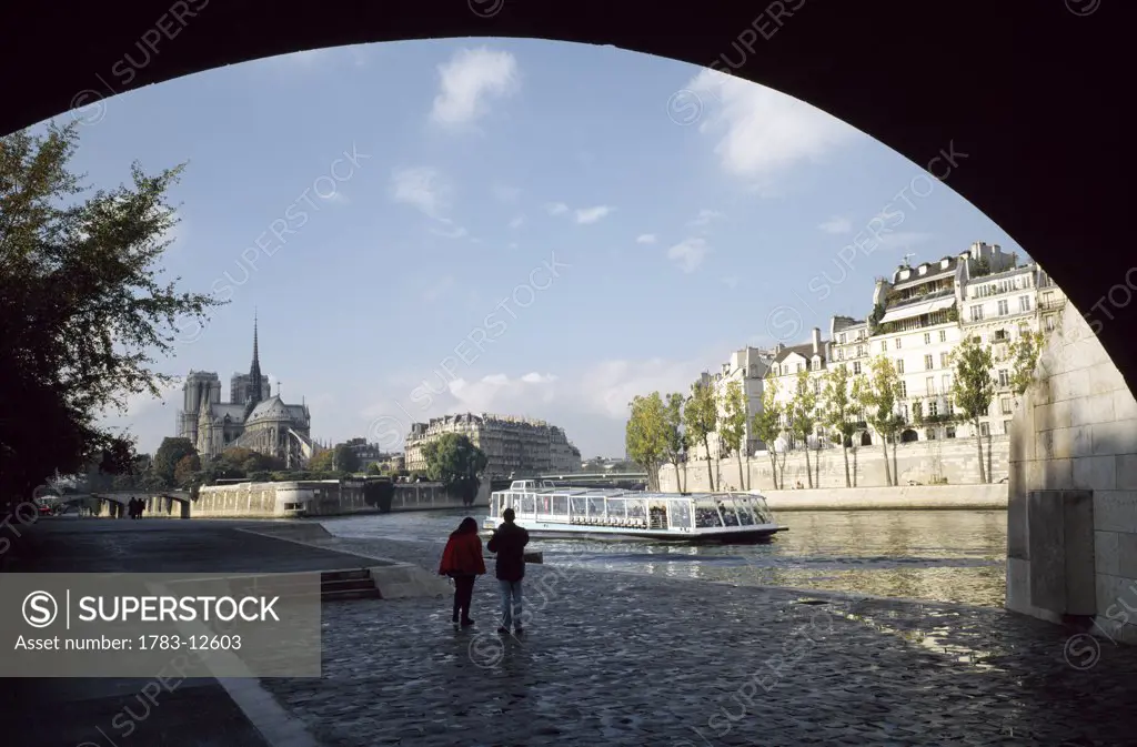 People walking under bridge near Notre Dame and River Seine, Paris, France.