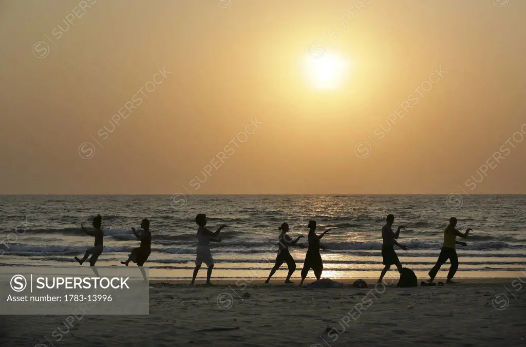 Silhouettes of people doing Tai Chi by the sea on the beach at sunset , Arambol , Goa , India 
