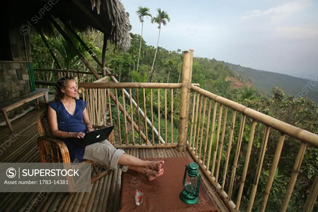 A  woman using a wireless laptop computer on the balcony of a remote bamboo hut, Near Mawlynnong, East Khasi Hills, Meghalaya, North East States, India