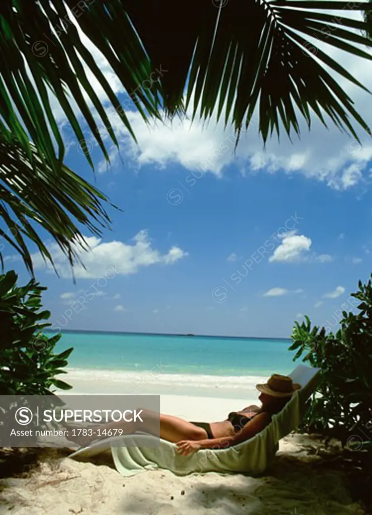 Woman lying on a sunlounger under palm trees, Praslin, Seychelles