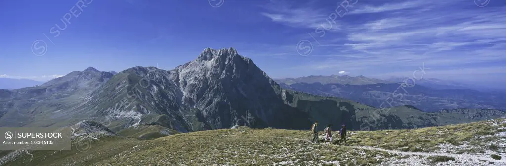Hikers going up ridge with corno grande behind, Campo Imperatore, Grand Sasso Park, Abruzzo, Italy 