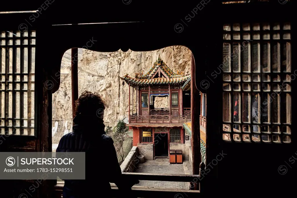 A tourist looking out a window at The Hanging Temple, also known as Hanging Monastery or Xuankong Temple, near Datong; China