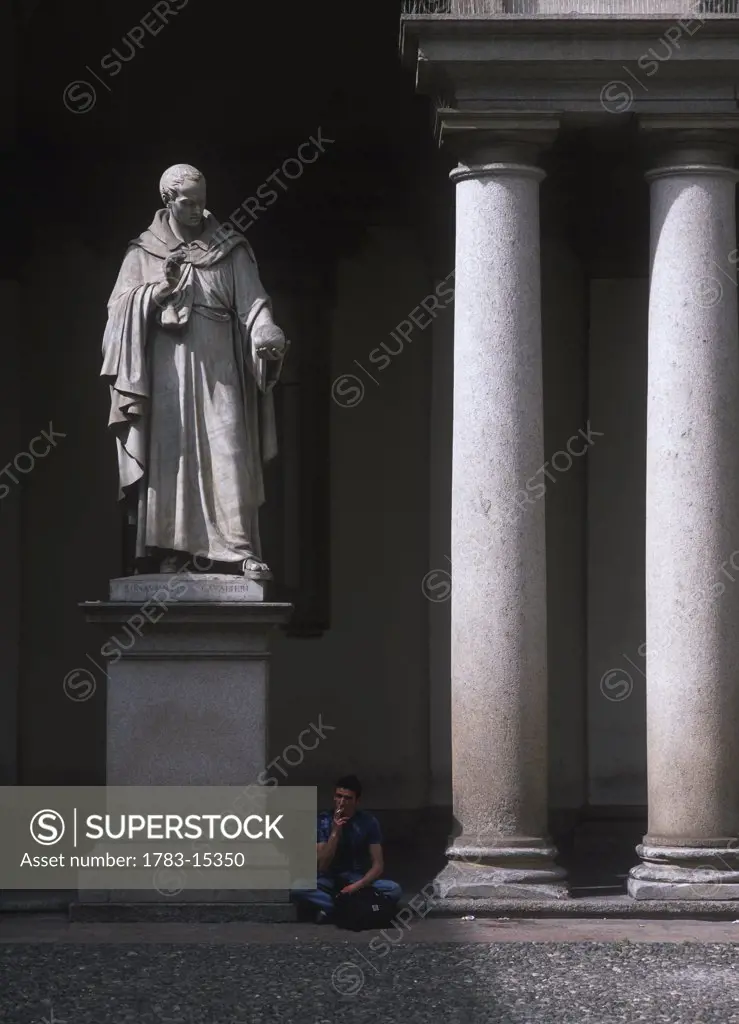 Man having cigarette beneath statue in the Pinocoteca di Brera art gallery, Milan, Italy.