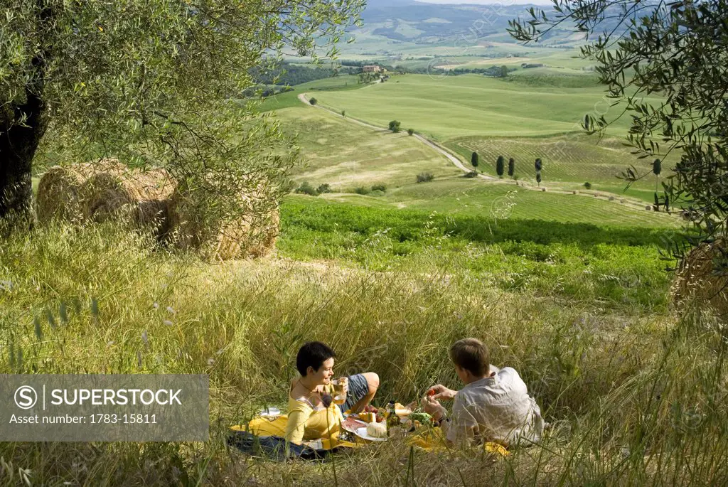Couple having picnic beside olive trees looking over the countryside, Tuscany, Italy