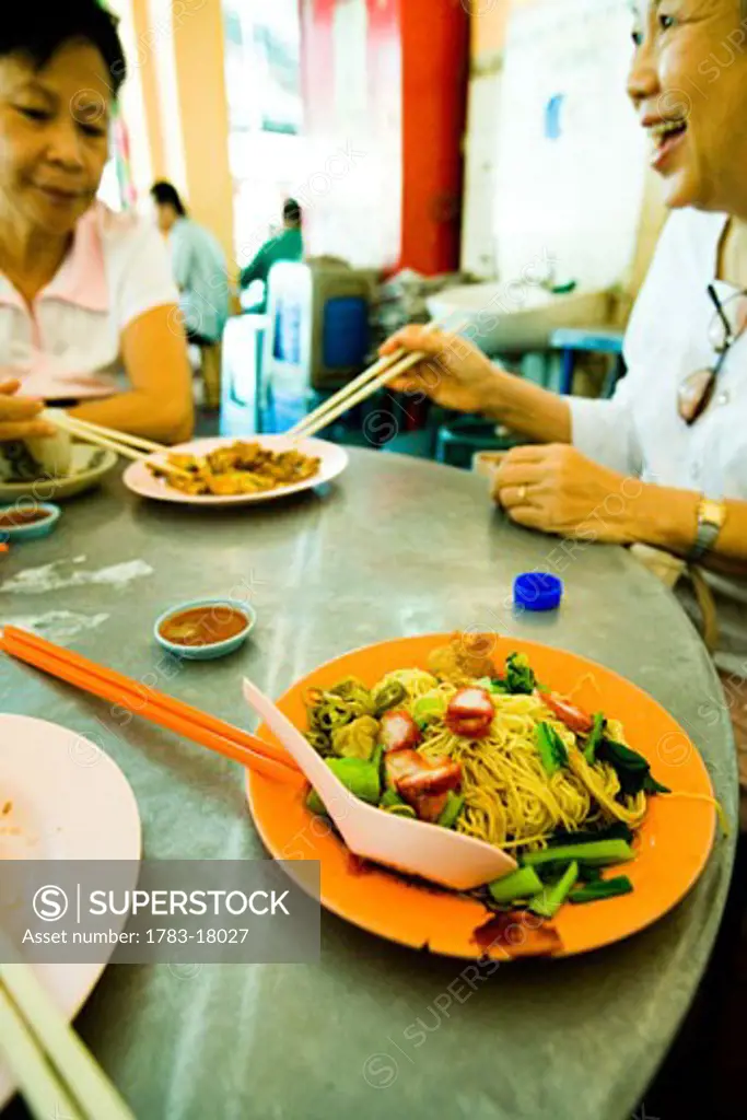 Chinese women eating fried oysters and noodle dishes, Georgetown, Pulau Pinang (Penang), Malaysia.
