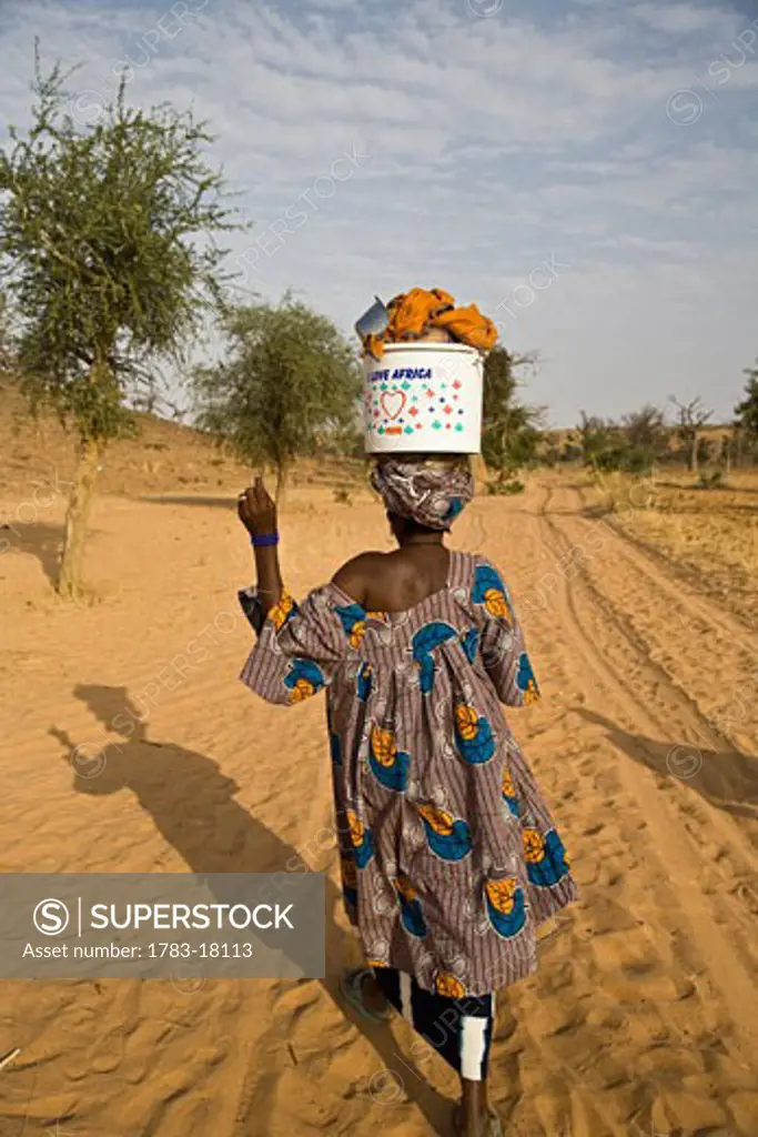 Woman walking with bucket on head at Bandiagara Escarpment, Dogon Country, Mali.