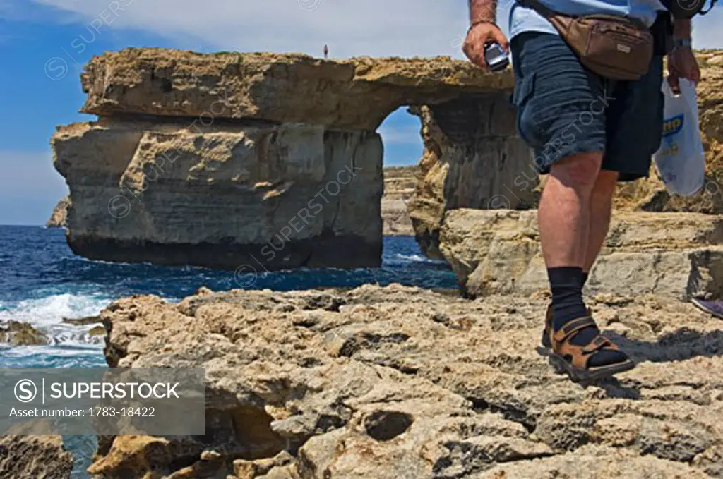 Male tourist walking on coastal cliff near Azure Window, low section, Dwejra Bay, Gozo Island, Malta.