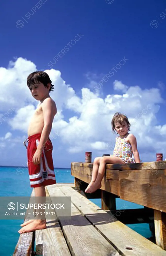 Boy and girl (4-7) relaxing on jetty, Mustique, St Vincent and the Grenadines.
