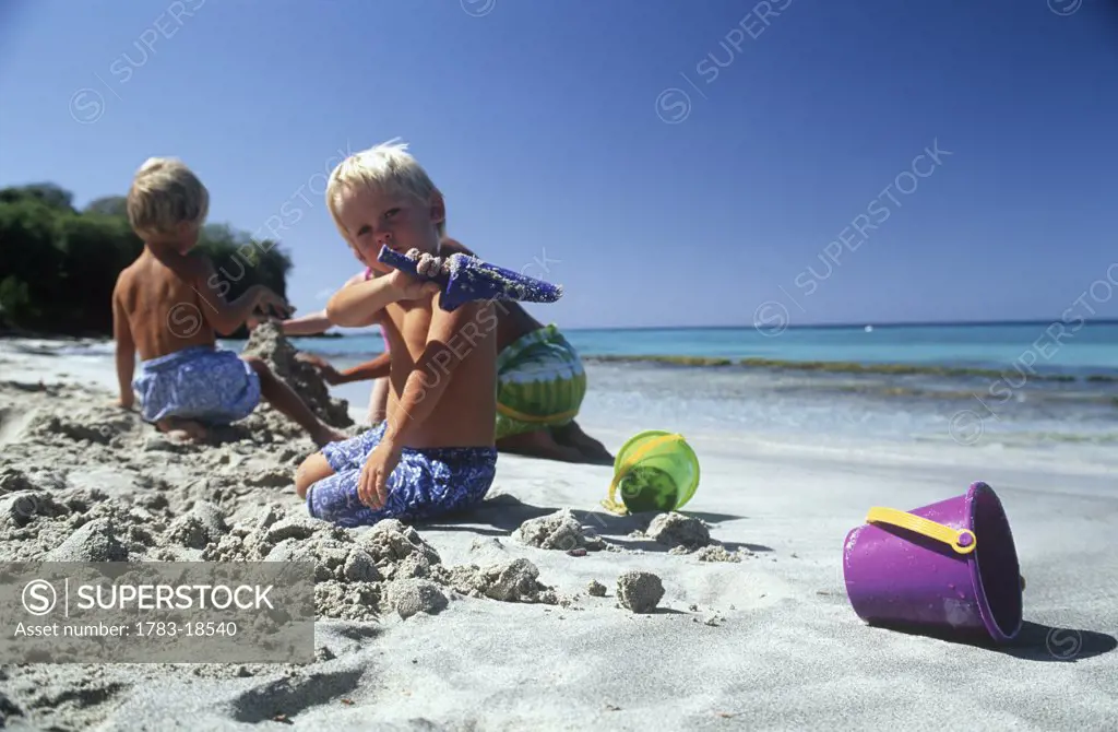 Children / family making sandcastles with buckets and spades,  Cotton House Beach, Mustique, West Indies.