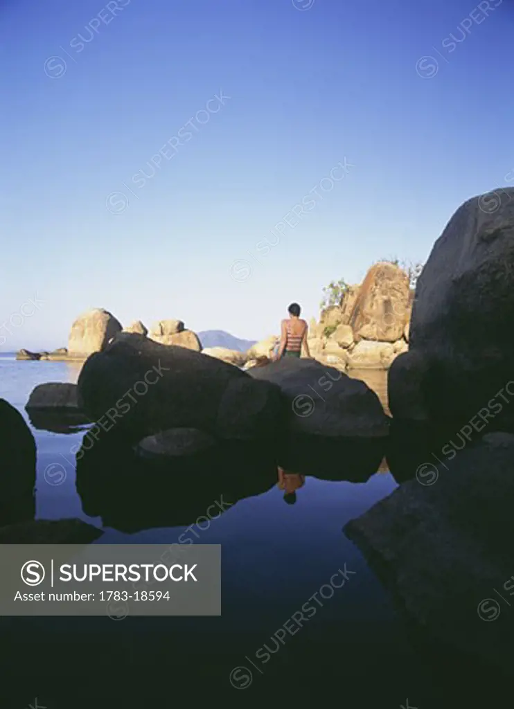 Woman sitting on rocks at dusk on Mumbo Island, Lake Malawi, Malawi