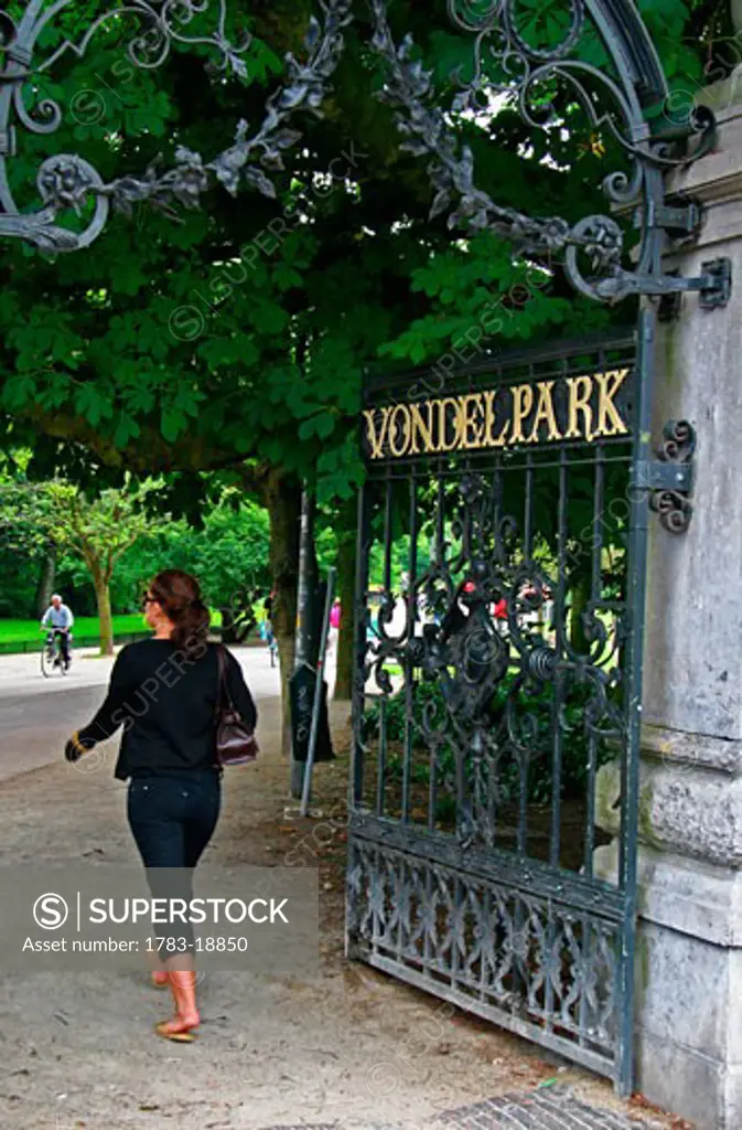 Young woman walking into entrance to Vondelpark, Amsterdam, Holland, The Netherlands
