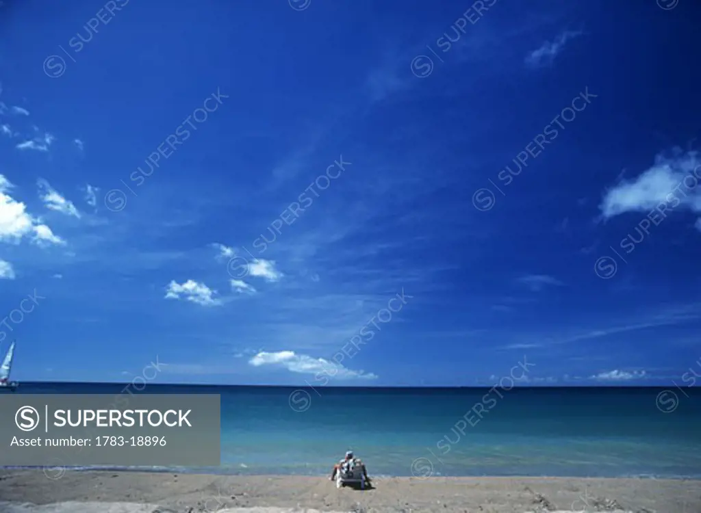 Tourist sun-bathing on idyllic sandy beach, Nevis Island.