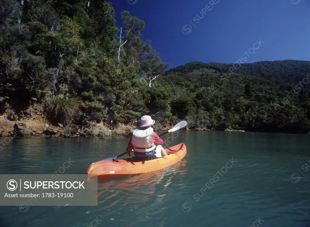 Woman kayaking past forest, Marlborough Sound, South Island, New Zealand.