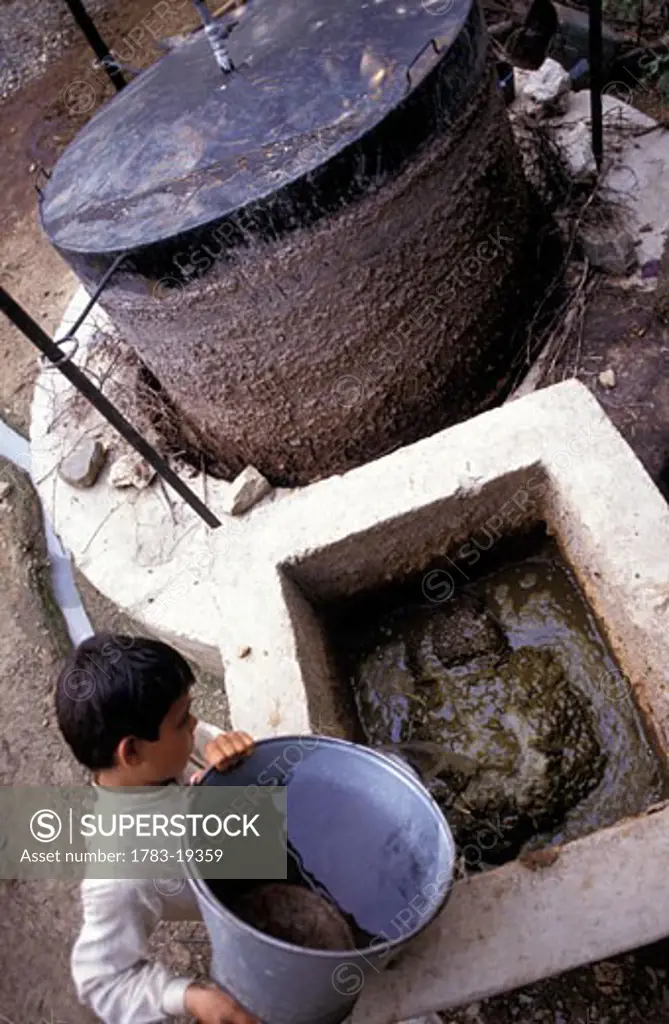 Boy working at Biogas generator with dung fuel, Pakistan.