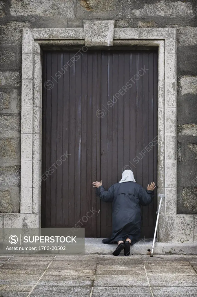 An old lady kneels in worship at the door of the Church , Muxia, Galicia, Spain