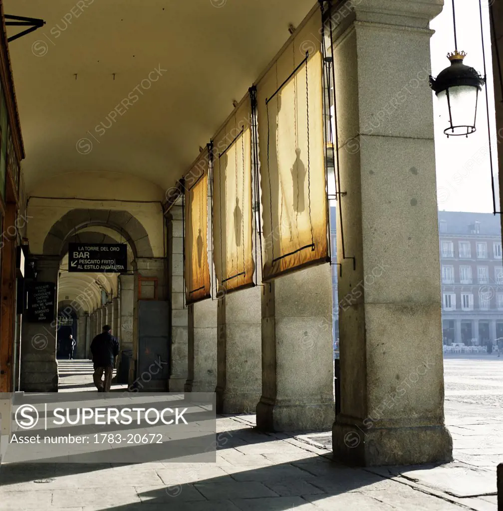 Man walking beside colonnade in Plaza Major, Madrid, Spain