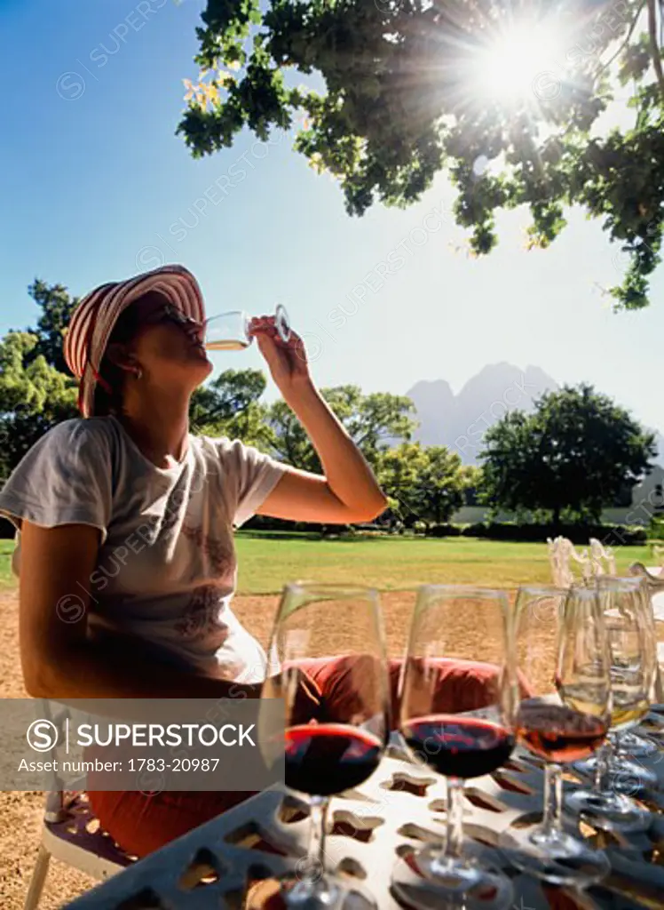 Woman tasting wine under oak tree at Boschendal wine estate, Stellenbosch, Western Cape, South Africa.