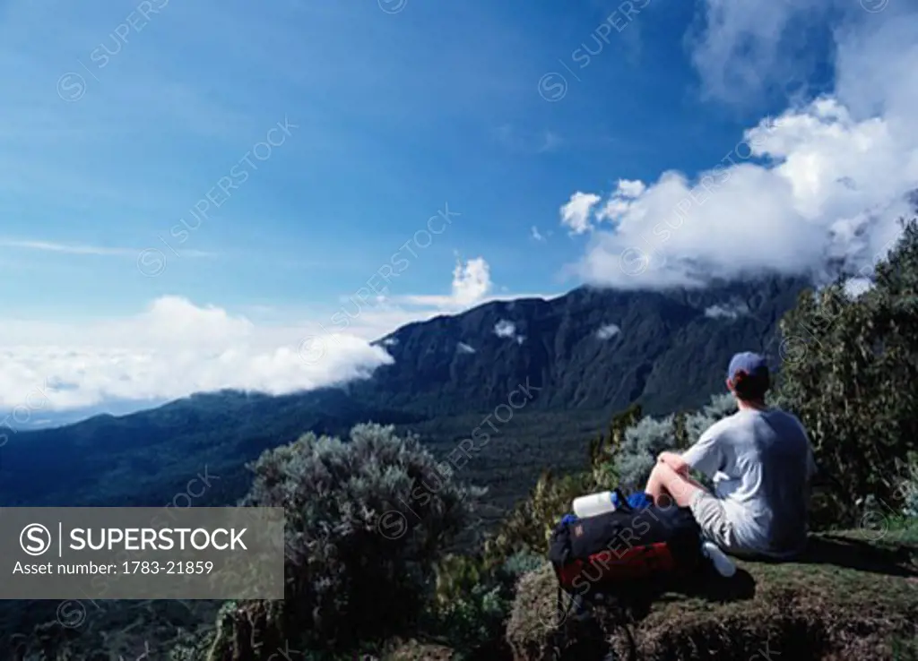 Woman with backpack sitting on edge of mountaintop, Mount Meru, Arusha National Park, Tanzania