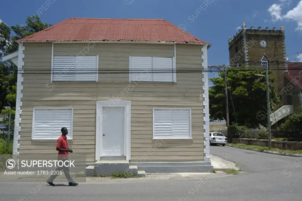 Man walking past old wooden house beside the church in Black River, Jamaica.                   