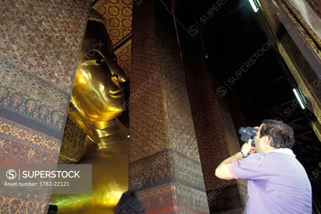 Tourist videoing huge reclining Buddha statue at Wat Po Temple, Bangkok, Thailand