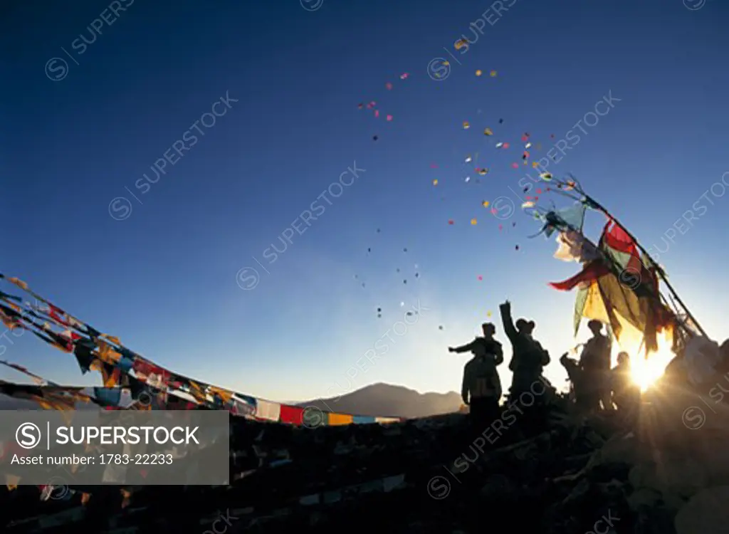 Pilgrims at dawn on hill beside prayer flags throwing windhorses into the air above Ganden Monastery for New Year, Tibet