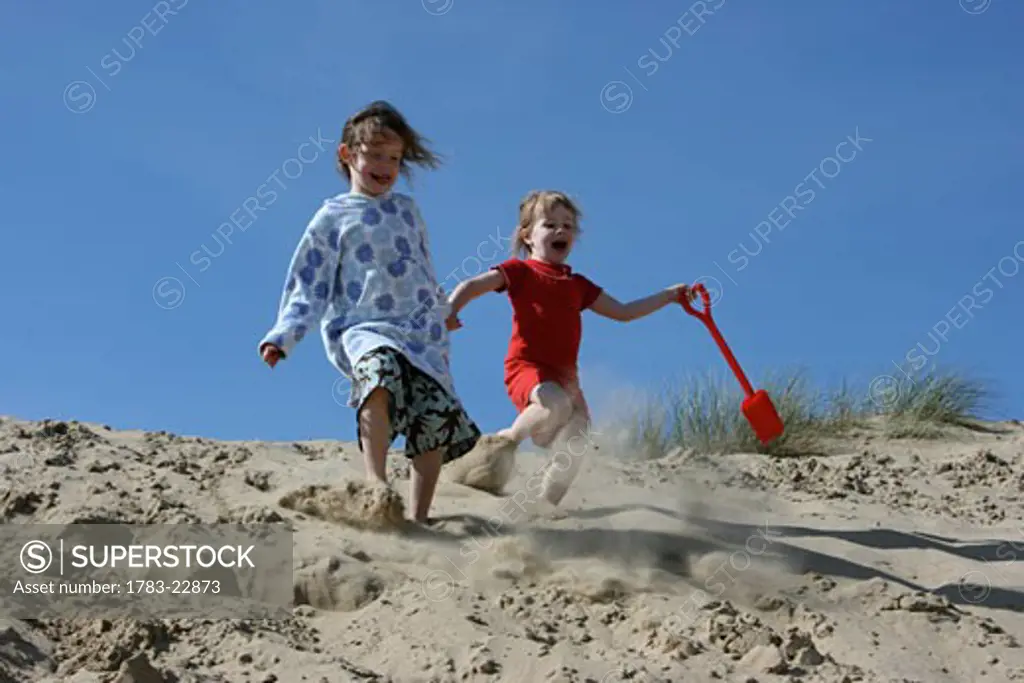 Sisters running down sand dunes holding hands, Camber Sands, Sussex. England