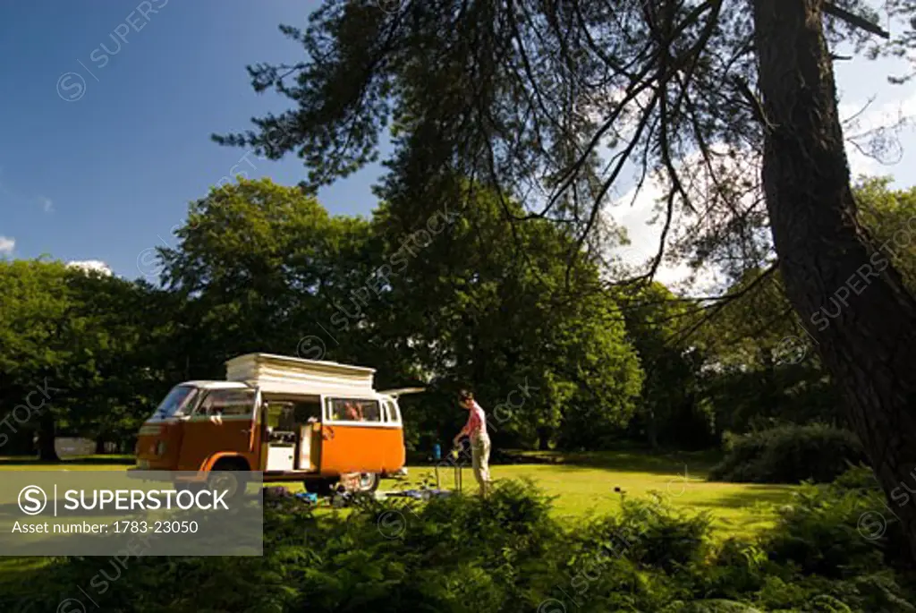 Woman making tea outside old campervan in forest clearing  , New Forest, Hampshire, UK