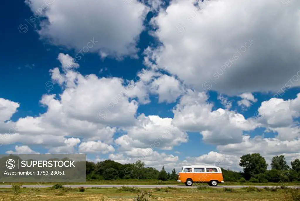 Old orange campervan driving through heathland , New Forest, Hampshire, UK