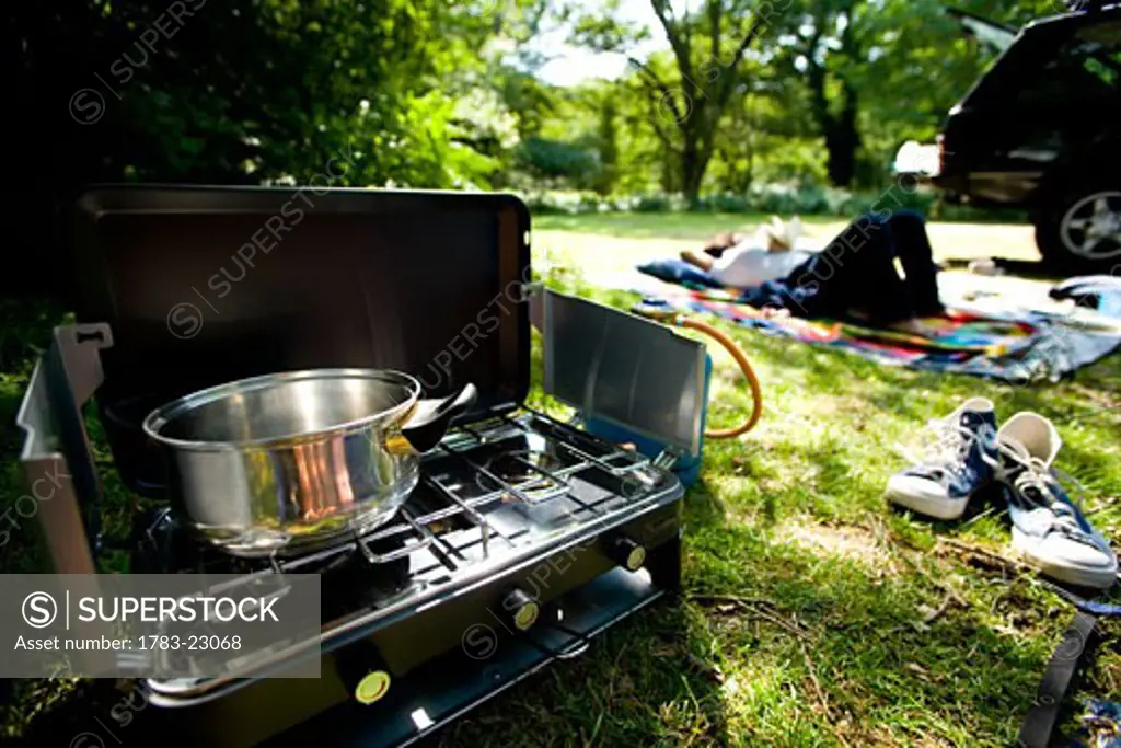 Woman lying down at campsite with stove in foreground, New Forest, Hampshire, England