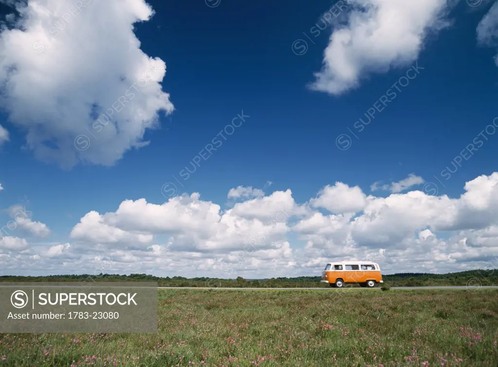 Campervan going down road in front of heather in flower , New Forest, Hampshire, England