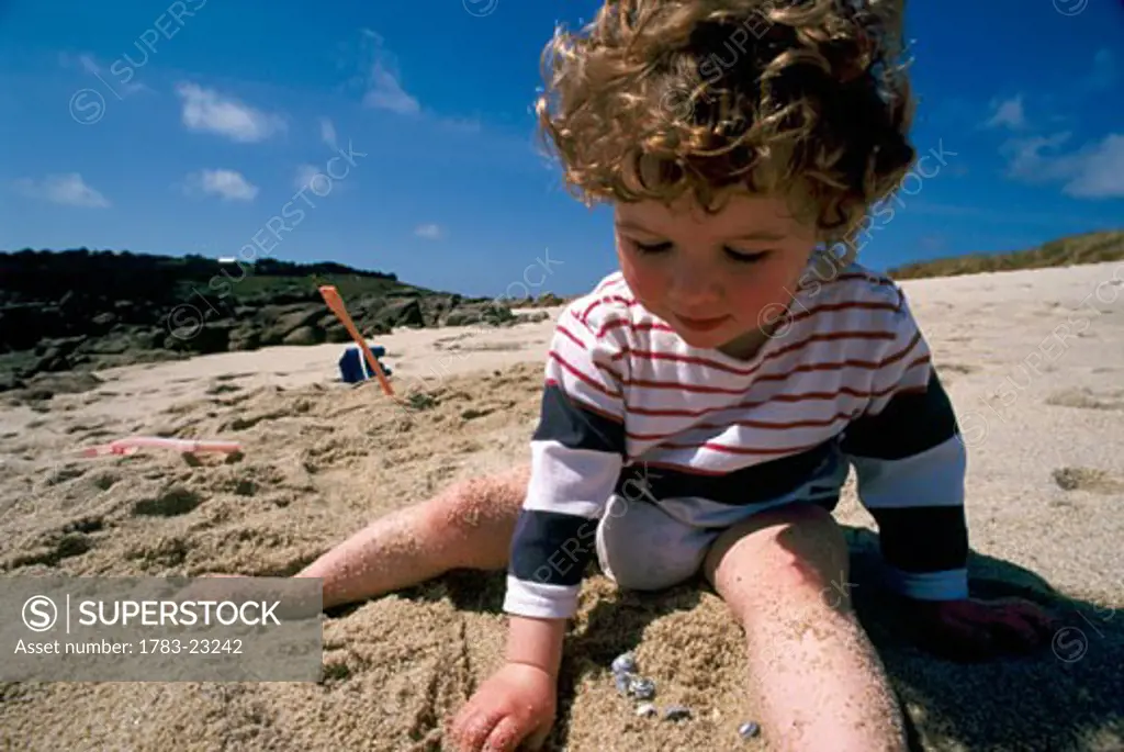 3 year old girl playing in sand on beach in the Scilly Isles, England