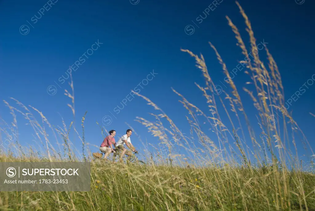 Couple going through meadow on tandem bicycle on the South Downs, Low Angle View, West Sussex, England