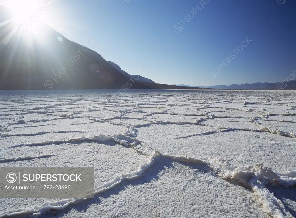Looking across the saltpans early in the morning with sun shining over mountain, Death Valley National Park, Badwater, California