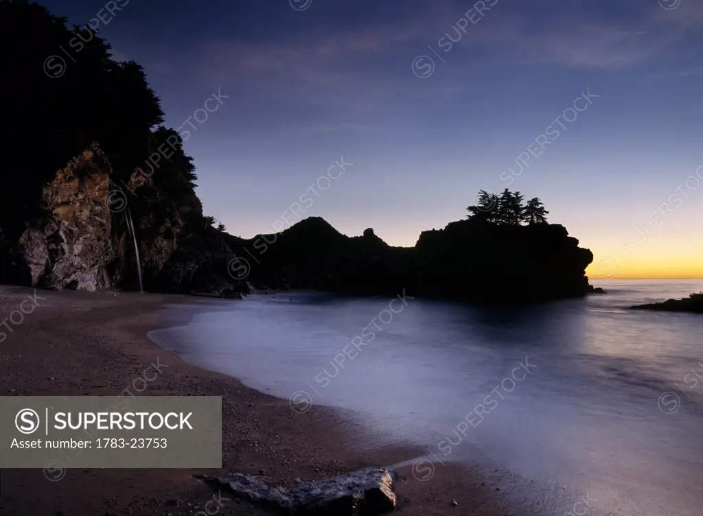 Looking out to sea at dusk from small beach with McWay Waterfall at end , Julia Pfeiffer State Park, Big Sur, California