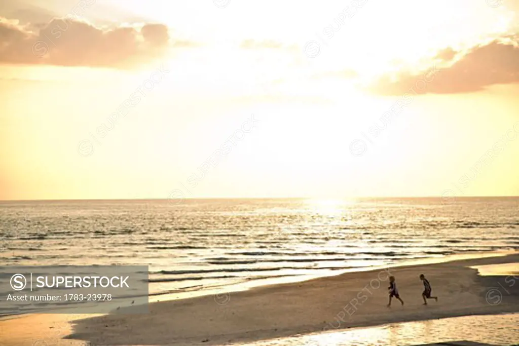 Two children running on beach at sunset, Sarasota, Florida, USA.