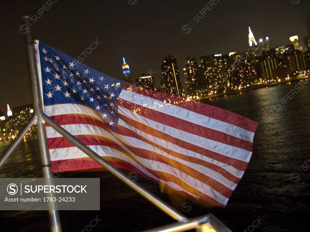 American flag in front of Manhattan skyline at night, New York City, New York State, USA.