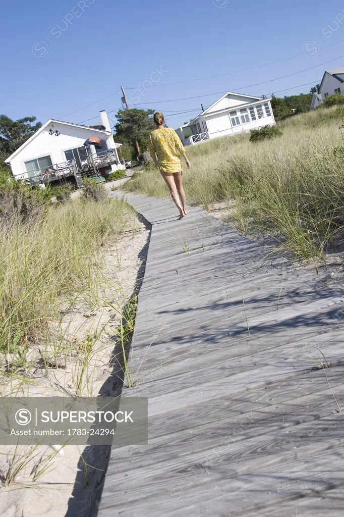 Woman in kaftan walking towards houses on beach wooden walkway, Peconic, North Fork, Long Island, New York
