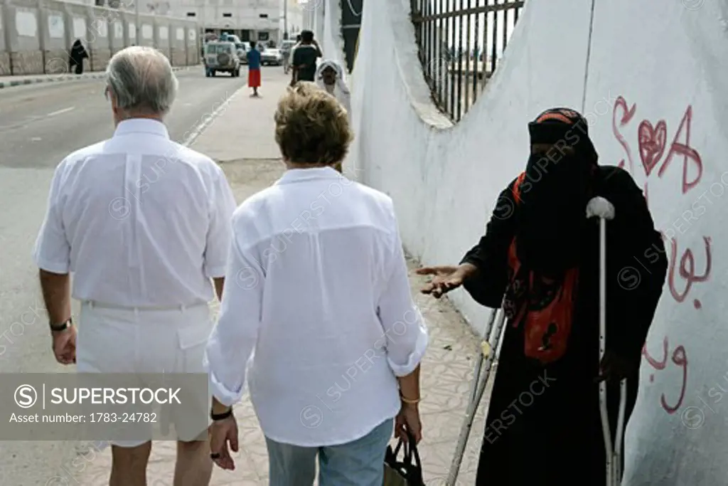 Elderly tourists ignoring a crippled woman begging as they pass, Mukalla, Gulf of Aden, Yemen