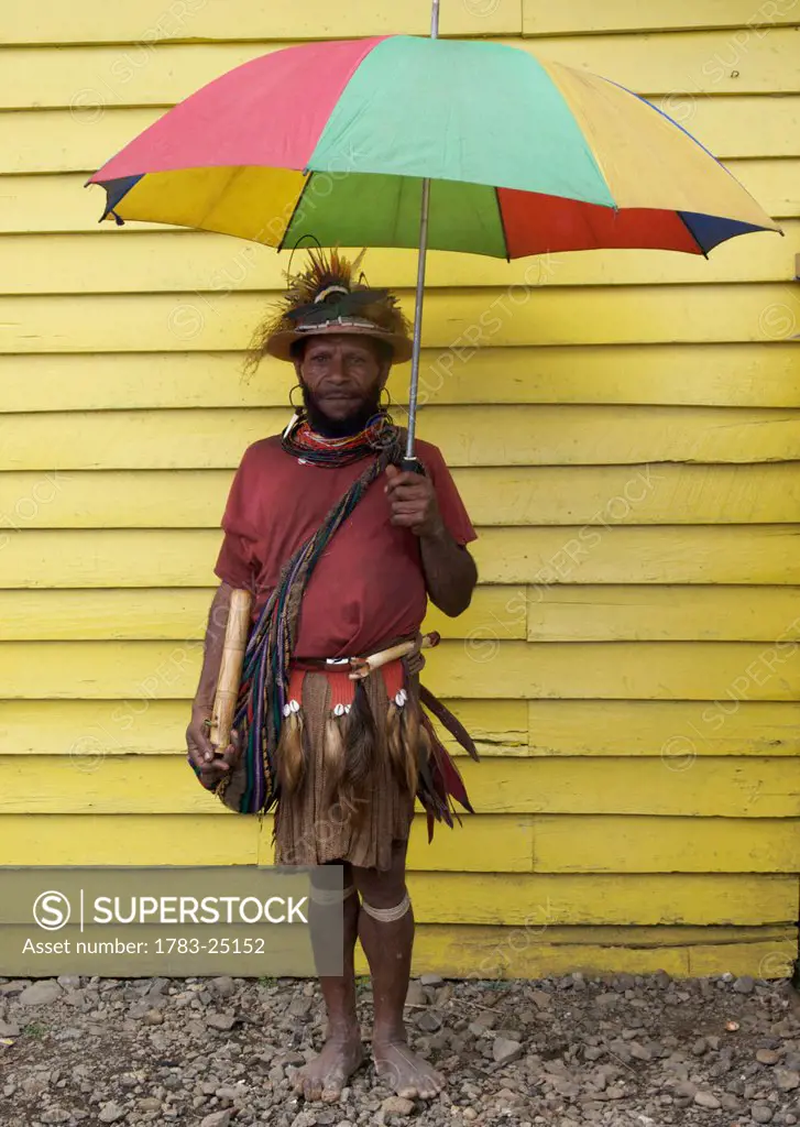 Villager standing under an umbrealla against a yellow building, Mount Hagen, Papua New Guinea.