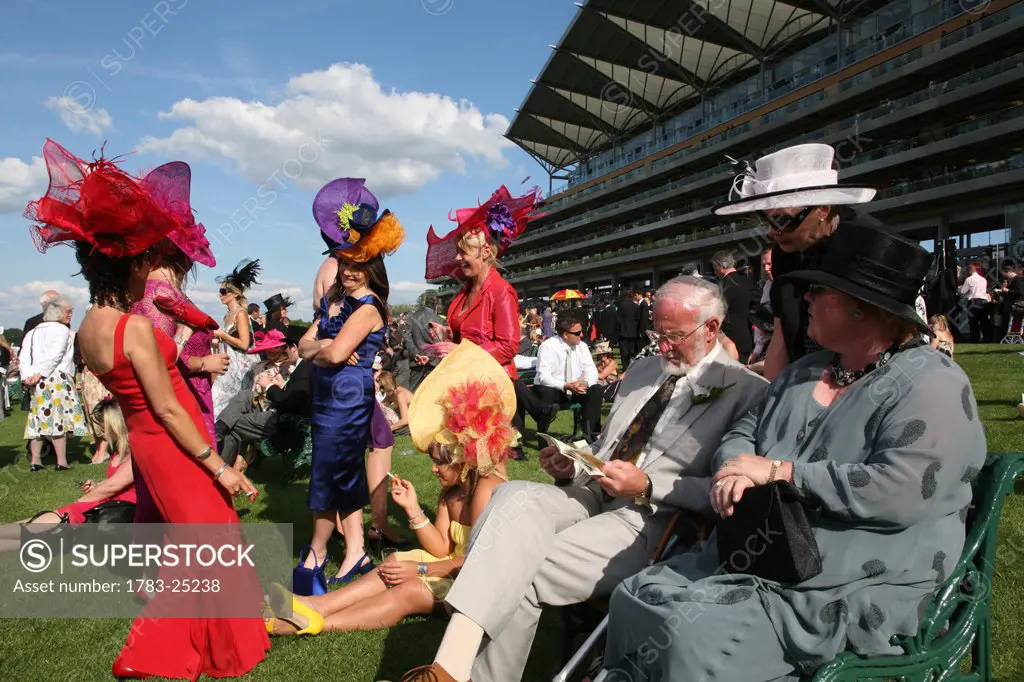 Women and men in hats and fashionable clothes at new Grandstand Enclosure during Royal Ascot horse racing meeting.