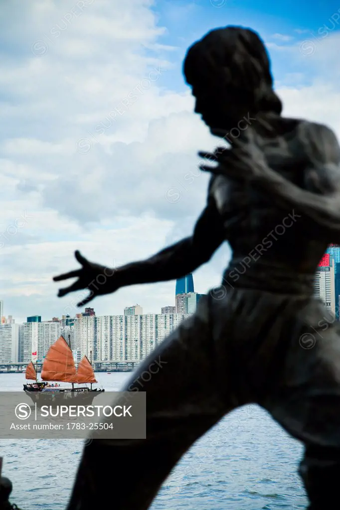 Traditional chinese Junk boat in background. Bruce Lee memorial statue, view of Victoria Harbour, Hong Kong Island skyline, from Tsim Sha Tsui, Kowloo...