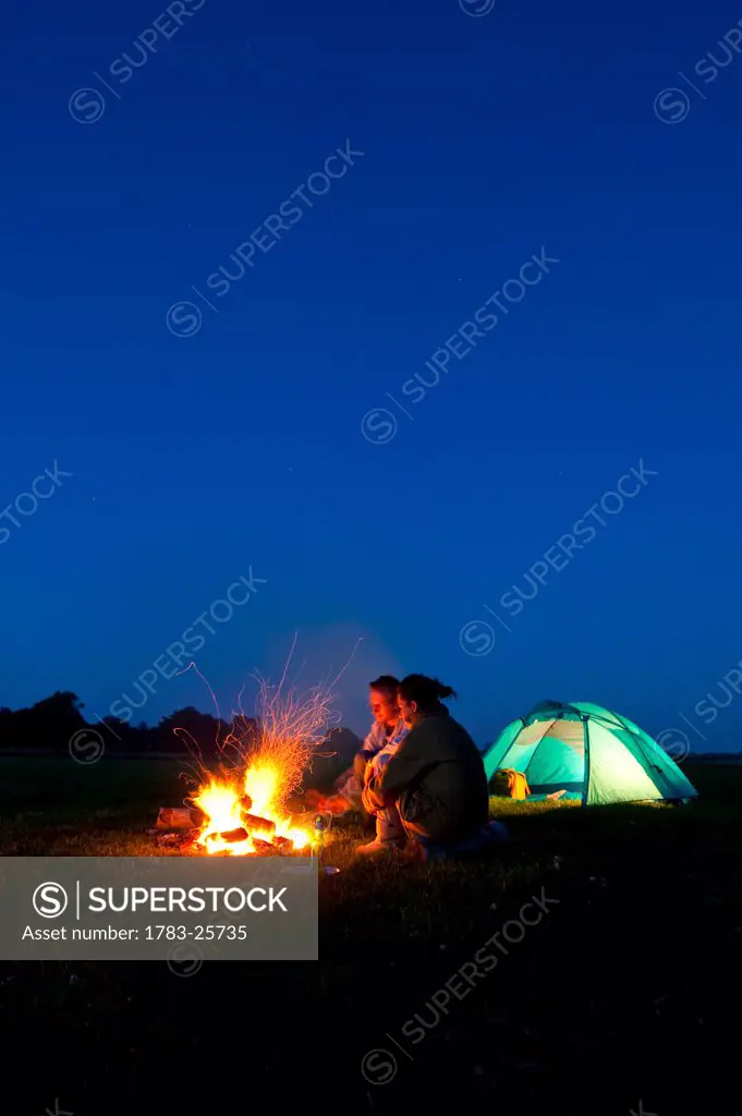 Couple camping with fire outside tent in field
