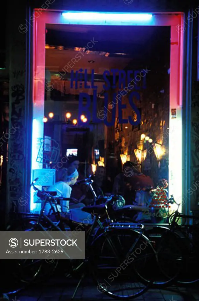 Hill Street Blues, trendy young people eating in a cafe / bar, bicycles, window front, neon lights.