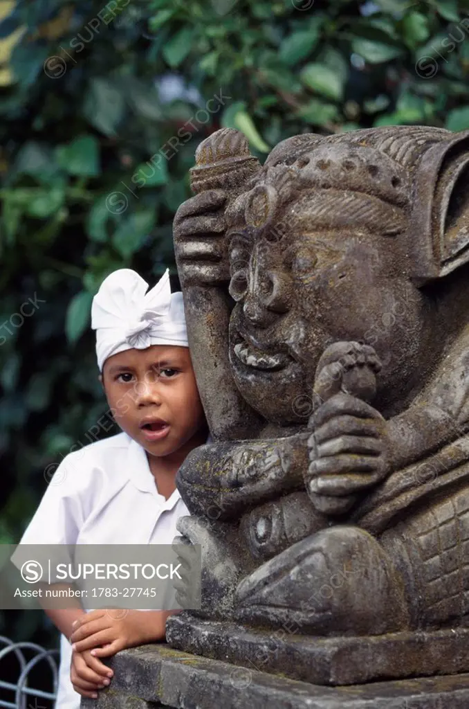 Boy with stone carved temple fighure, Bali, Indonesia.