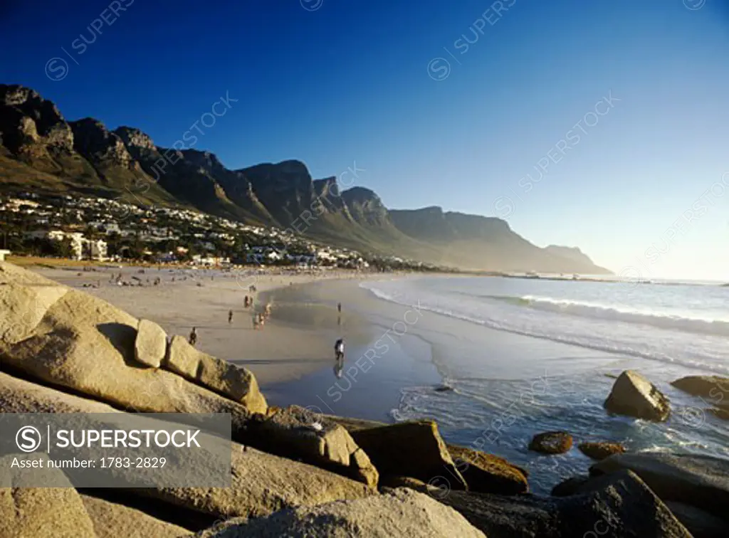 People walking along Camps Bay beach at dusk with The 12 Apostles behind, Cape Town, South Africa.    
