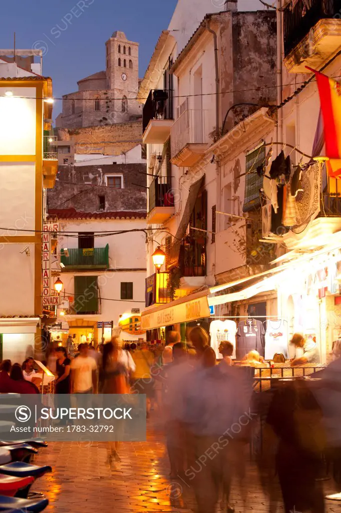 People in alleys at dusk with Santa Maria cathedral on hill behind, Ibiza Town, Ibiza, Spain