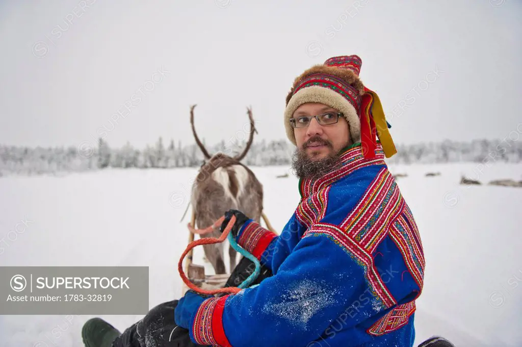 A Herder Wearing The Traditional Sami Clothing With Reindeer At Ounaskievari Reindeer Farm, Levi, Lapland, Finland